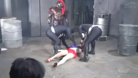 Asian Girl in Red Costume with Males in Industrial Setting