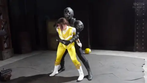 Asian Woman in Yellow Superhero Costume Fights in Dark Setting