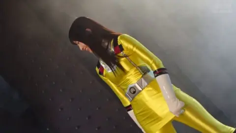 Asian Woman in Yellow Bodysuit in Industrial Setting