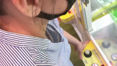 Asian Teen Plays Claw Machine in Striped Shirt