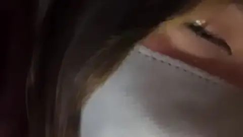 Asian teen with mask lies on purple bed sheets