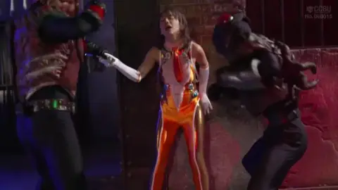 Captive Brunette in Orange Costume