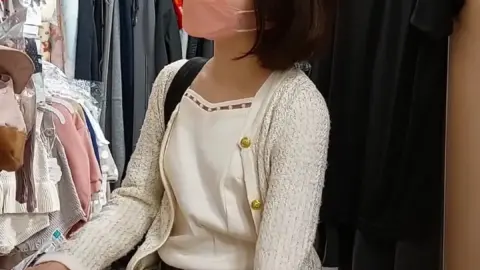 Asian teen in pink face mask kneeling in clothing store