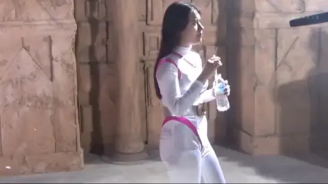 Woman in White Jumpsuit Interacts with Crew and Performs