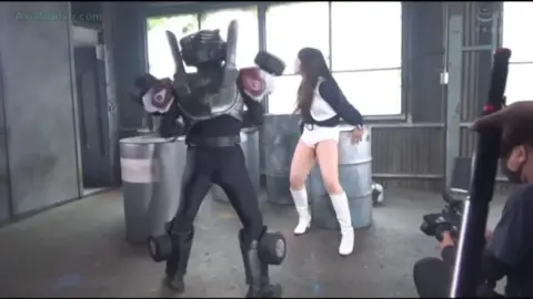 Asian Performer in White Boots and Shorts in Industrial Setting